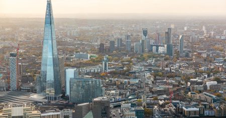 Aerial view of the london skyline, highlighting skyscrapers, surrounding buildings, the river Thames, and a cloudy sky